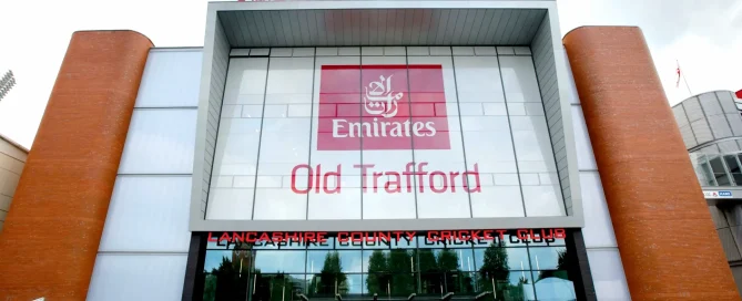 The Emirates Old Trafford cricket stadium facade featuring large red and white branding on glass windows.