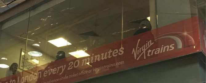 Red Virgin Trains window advertisement on perforated film, showcasing 20-minute travel times to London.