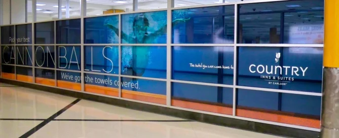 Country Inns and Suites brand advertisement featuring a child swimming underwater on airport glass partition walls.