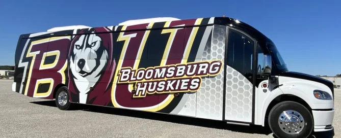 Bloomsburg Huskies coach bus with a full-body vinyl wrap displaying a husky mascot and branding.