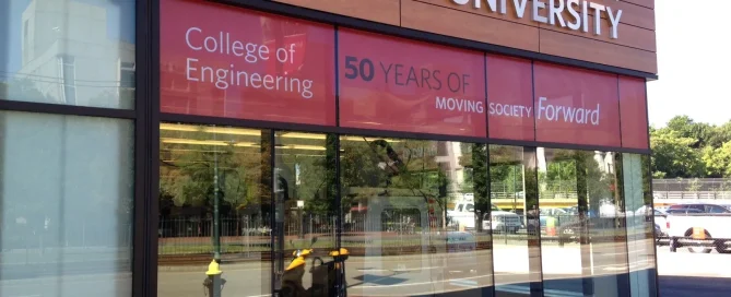 Boston University College of Engineering exterior with red 50 Years Moving Society Forward window graphics.