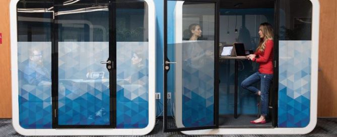 Employees working in two acoustic booths with blue and white geometric privacy film.