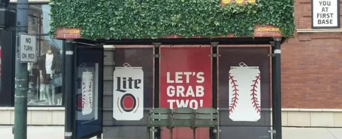 A bus shelter wrapped with Chicago Cubs and Miller Lite branding, featuring a green ivy roof and Let's Grab Two slogan.