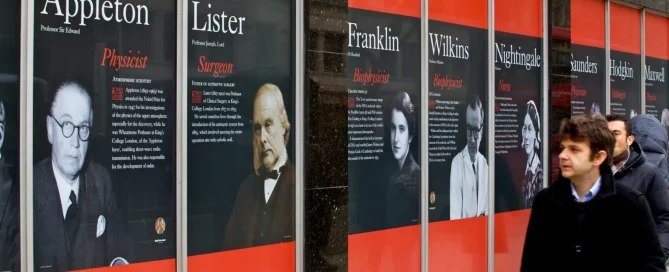 Street-level view of King's College London wall display featuring large portraits and profiles of historical scientists.