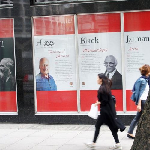Kings College London exterior windows with biographical graphics of Higgs and Black featuring portraits and text.
