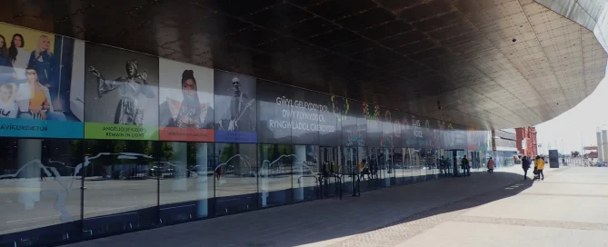 Wales Millennium Centre glass facade with colourful event graphics along ground-level windows.