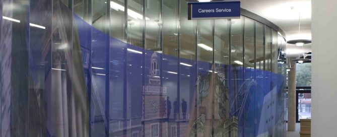 Curved glass corridor at Newcastle University featuring blue privacy window film and a Careers Service sign.