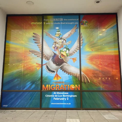 Animated ducks flying on a colourful Migration movie poster wrapped on cinema glass windows.