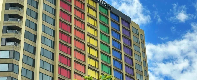 A tall hotel building with rows of windows covered in vibrant rainbow-coloured film for a pride celebration.