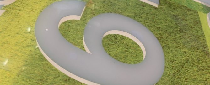 Close-up of a white, 3D-effect number 6 numeral applied to a green, grass-textured background.