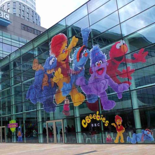 BBC CBeebies building at MediaCityUK featuring large character graphics on perforated window films.
