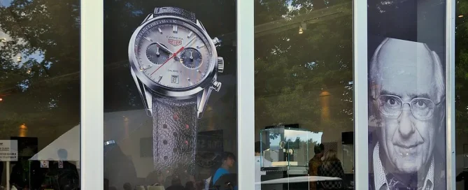 TAG Heuer display featuring a wristwatch graphic and portrait on perforated window film at a public event.