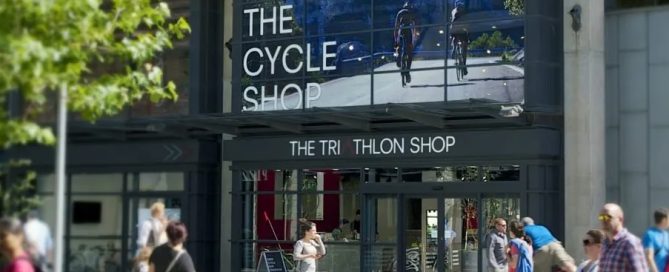 Exterior of The Cycle Shop featuring large, branded perforated window film graphics showing cyclists.