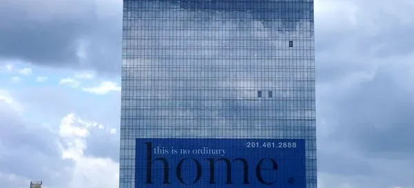 Giant blue perforated building wrap advertising luxury apartments on the glass facade of The Modern skyscraper.