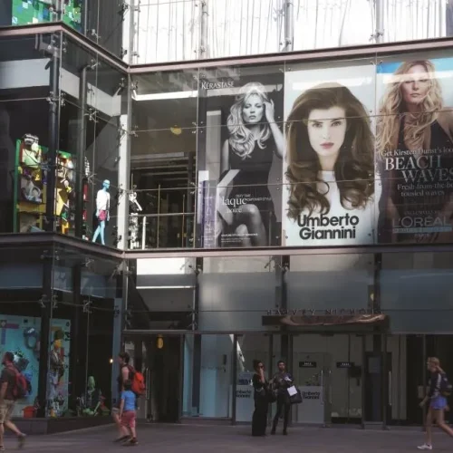 Harvey Nichols storefront with large beauty product campaign imagery featuring models displayed on glass windows.
