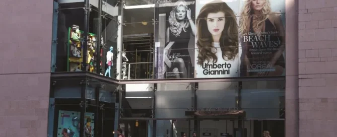 Harvey Nichols storefront with large beauty product campaign imagery featuring models displayed on glass windows.