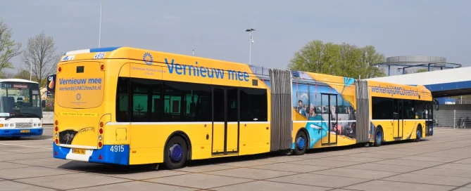 A long, bright yellow articulated bus in Utrecht featuring full-body wrap and perforated branding on the windows.