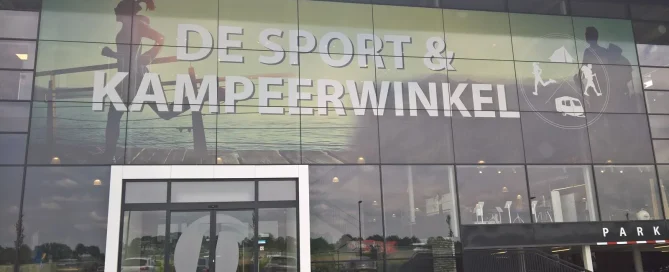 Modern exterior of Van Duinkerken sports and camping shop, featuring large perforated window film advertisements.