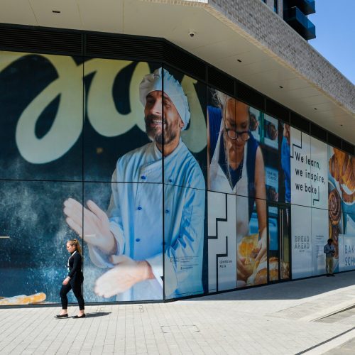 Person walking past large glass window graphics of a baker at a Wembley Park store.