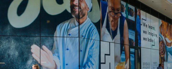 Person walking past large glass window graphics of a baker at a Wembley Park store.
