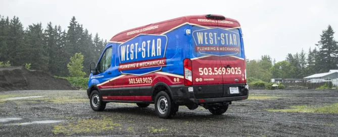 A blue and red West Star Plumbing and Mechanical service van parked on a gravel ground with trees in the background.