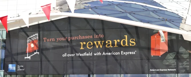 A Westfield shopping centre facade featuring a large American Express advertisement for rewards with red and white bunting.