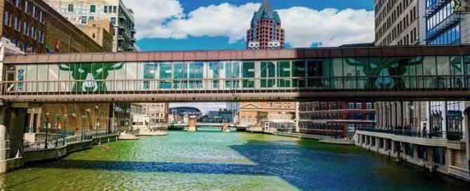 A pedestrian footbridge over a river in Milwaukee with window graphics displaying the Milwaukee Bucks logo.