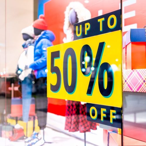 Retail window display featuring a yellow sign advertising an up to 50 percent off sale near mannequins.