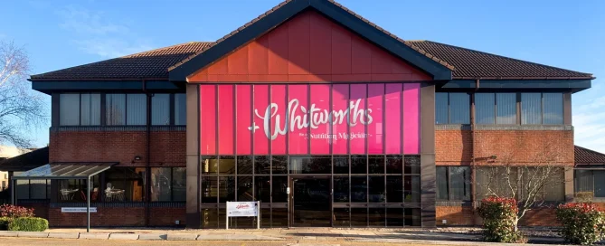 Whitworths head office featuring vibrant pink branded window graphics applied to large facade glass panels.