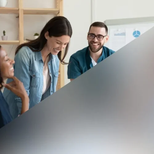 Office colleagues laughing during a meeting behind a medium frosted glass partition that provides semi-privacy.
