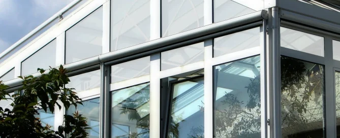 White-framed conservatory against a blue sky with clouds, featuring glass panels treated with Contra Vision film