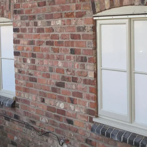 Cream-framed house windows featuring microperforated one-way privacy film against a rustic red brick wall.